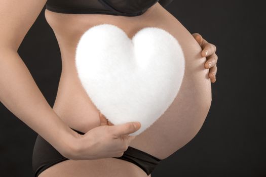 Profile of a pregnant woman holding white heart on her abdomen.