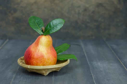 Ripe red pears with green leaves on basket over wooden table