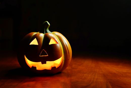 Illuminated Halloween smiling spooky pumpkin on a dark background.