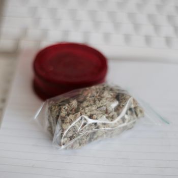 Red grinder, marijuana in big transparent bag near white computer keyboard.