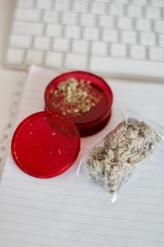 Red grinder, marijuana in big transparent bag near white computer keyboard.