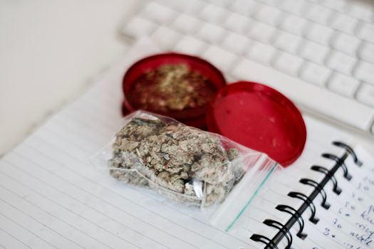 Red grinder, marijuana in big transparent bag near white computer keyboard.