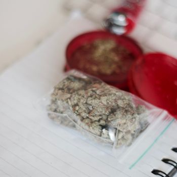 Red grinder, marijuana in big transparent bag near white computer keyboard.