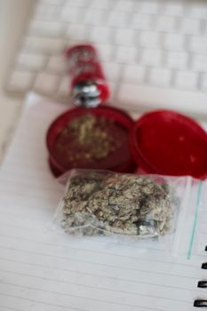 Red grinder, marijuana in big transparent bag near white computer keyboard.