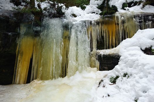 Frozen waterfalls on the rock, orange colored and snow