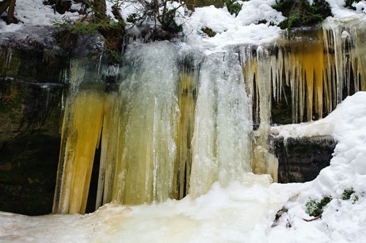 Frozen waterfalls on the rock, orange colored and snow