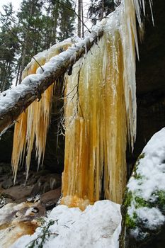 Frozen waterfalls on the rock, orange colored and snow