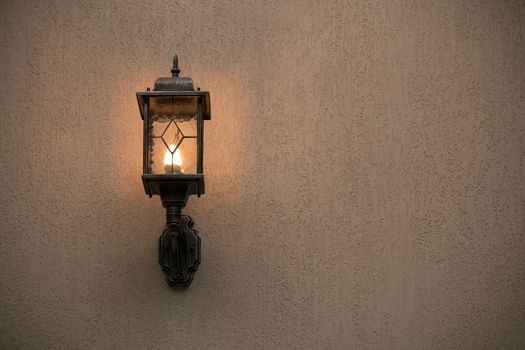 A yellow glass lantern hanging on a gray old wall. Bright glowing lantern illuminating the wall of an ancient building.