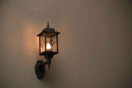 A yellow glass lantern hanging on a gray old wall. Bright glowing lantern illuminating the wall of an ancient building.