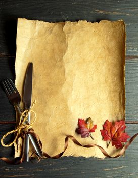 Empty paper scroll with fork and knife tied with ribbon bow and autumn leaves