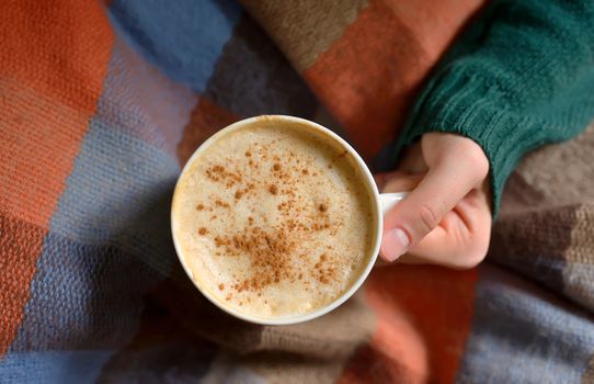 Girl with cup of cappuccino coffee on blanket 