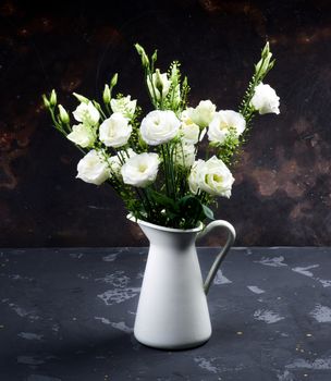 Elegant Flowers Bouquet with White Lisianthus and Decorative Green Stems in White Tin Jug closeup on Dark Grunge background