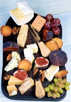 Gourmet Cheese Plate with Brie, Parmesan, Roquefort, Camembert and Herve Cheese, Figs and Grape with Biscuits on Slate Plate closeup on Wooden background. Top View