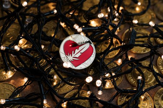 Digital currency physical metal gold feather coin near the light. Christmas cryptocurrency concept.