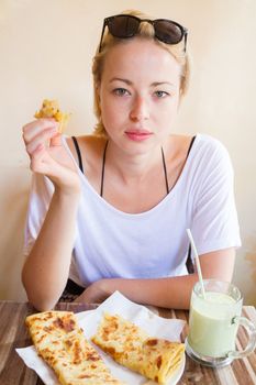 Female tourist eating delicious moroccan brakfast at one of street coffee shops: traditional pancakes with cheese and honey and avocado milkshake.