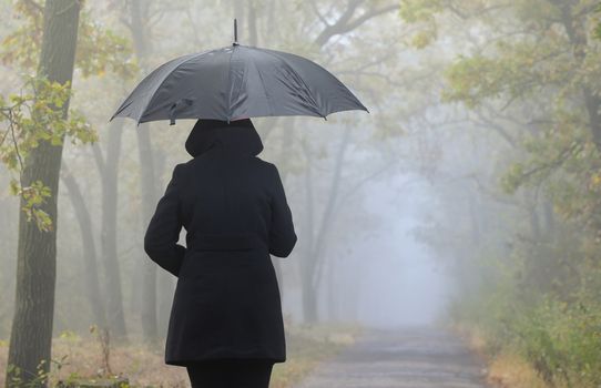 Depressed woman with red umbrella and foggy forest