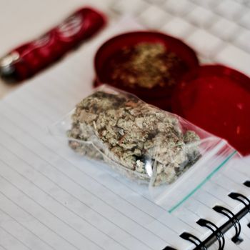 Red grinder, marijuana in big transparent bag near white computer keyboard.