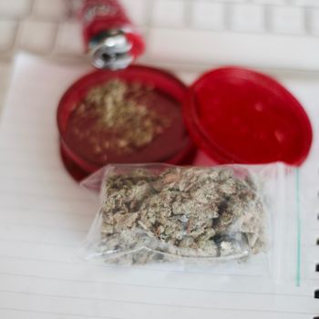 Red grinder, marijuana in big transparent bag near white computer keyboard.
