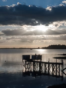 sunset over boat pier dock wooden structure jetty in river lake clouds dramatic; essex; england; uk