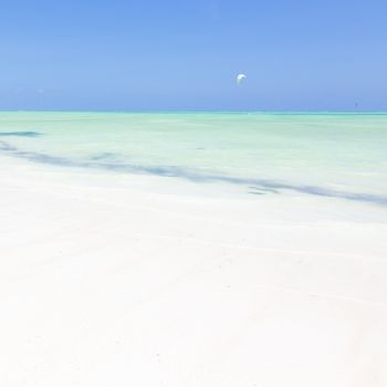 Solitary kite surfer kite surfing on picture perfect white sandy beach with turquoise blue sea, Paje, Zanzibar, Tanzania. Copy space.