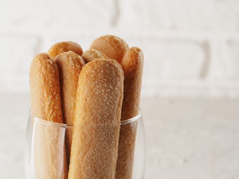 Close up view of ladyfinger biscuit cookie in glass jar on white brick wall background. Italian cookie savoiardi. Copy space.