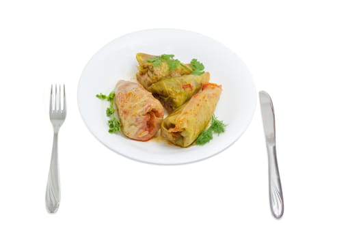 Several cooked cabbage rolls, twigs of parsley, dill and cilantro on white dish, fork and knife beside on a light background
