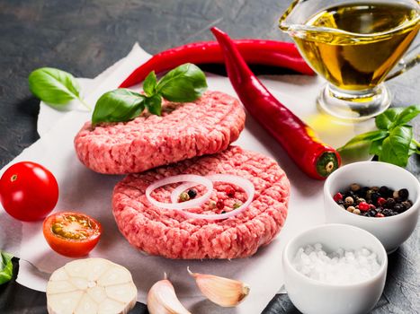 Close up view of two raw meat steak cutlets for burger with vegetables, spices, fresh basil, olive oil. Making homemade burger.