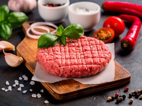 Close up view of two raw meat steak cutlets for burger with vegetables, spices and fresh basil. Making homemade burger.