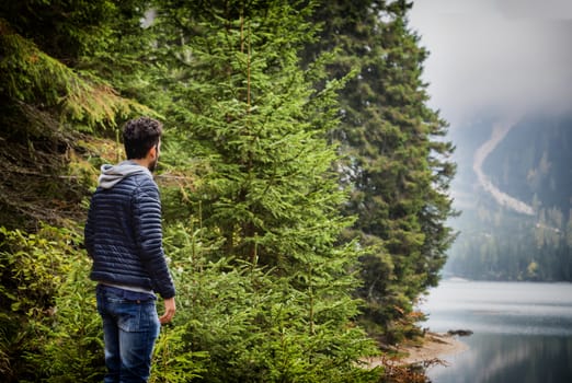 Handsome yung man standing on background of woods on shore of lake looking away.