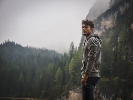 Handsome yung man standing on background of woods looking away.