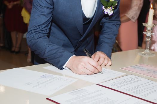 Young couple signing wedding documents. Focus on hand.