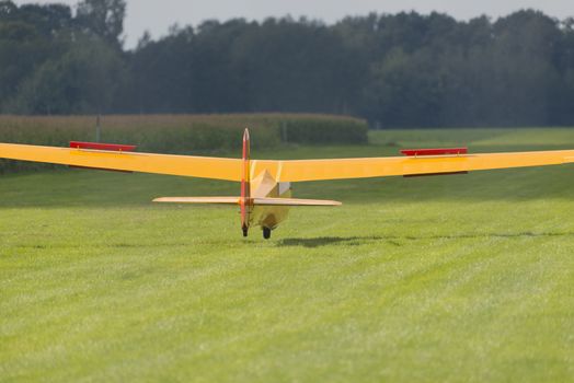Yellow glider in landing just before the head wheel hits the grass field
