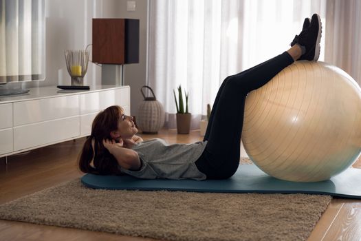 Full length shot of a woman doing exercise at home with a swiss Ball