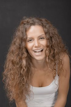 A young beautiful female with gorgeous hair laughing to camera. Studio shot.
