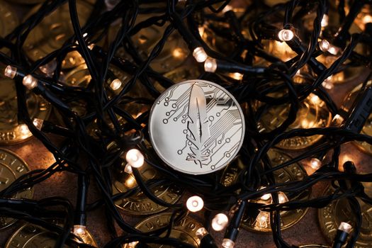 Digital currency physical metal gold feather coin near the light. Christmas cryptocurrency concept.