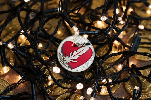 Digital currency physical metal gold feather coin near the light. Christmas cryptocurrency concept.