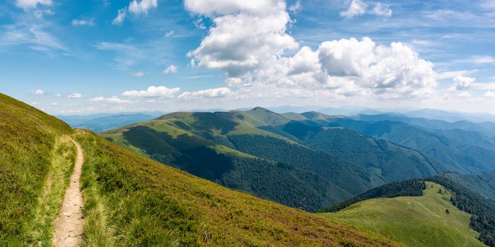 beautiful mountainous landscape on fine summer day. footpath running through grassy hillside under blue sky fluffy clouds. gorgeous panorama of mountain ridge