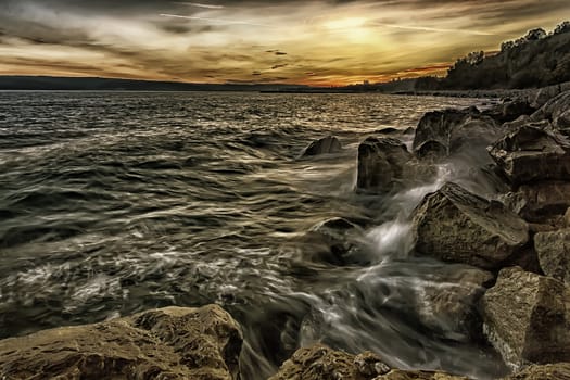 Sunset over the sea with splash waves on the rocks