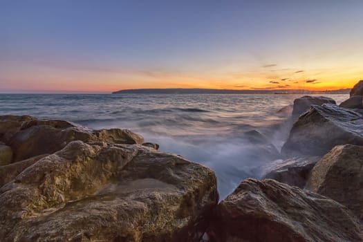 Sunset over the sea with splash waves on the rocks