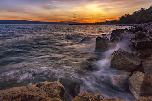 Sunset over the sea with splash waves on the rocks