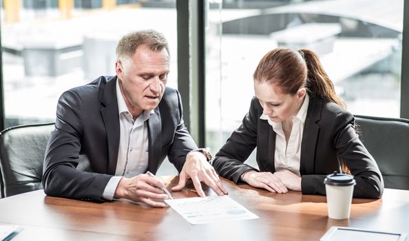 Mature business man and his young female assistant sitting at meeting table in office