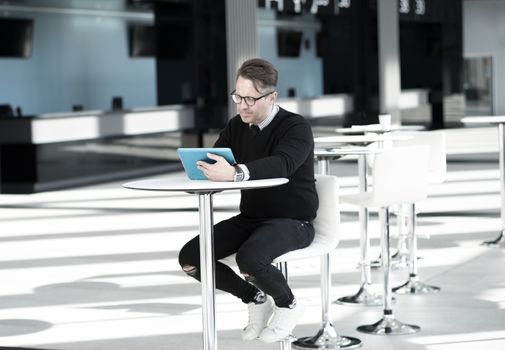 Mature man sitting in cafe of modern office building and using tablet