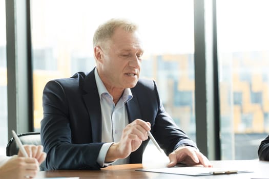 Mature business man sitting at meeting table in office and talking