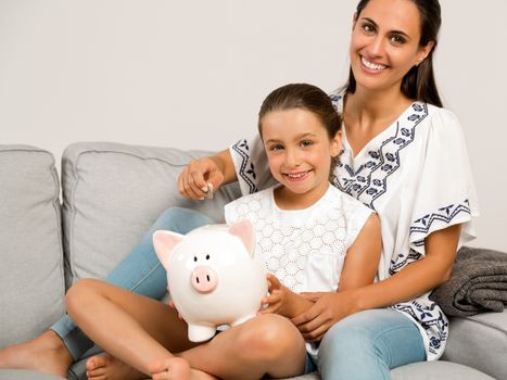 Mother and daughter putting coins into a piggy bank