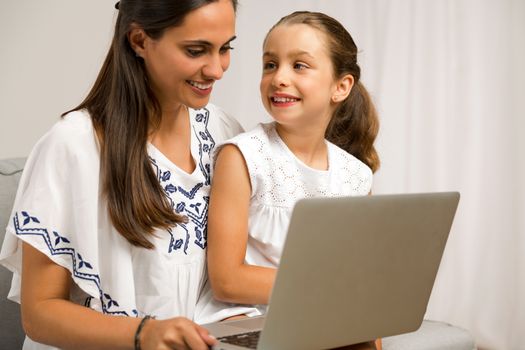 Mom teaching Daughter working with a a laptop at home