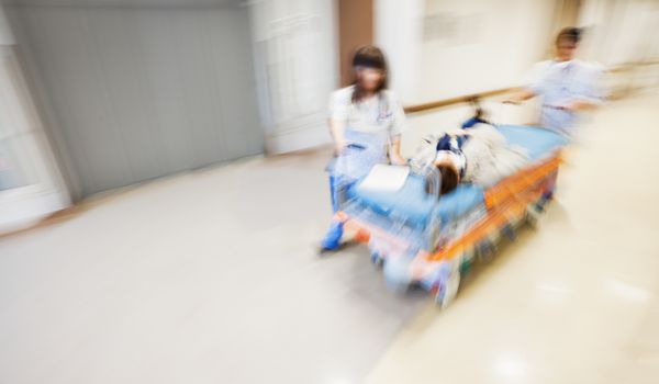 An emergency litter with patient, pushed fast through modern hospital corridor by two nurses. Panned, motion blurred picture.