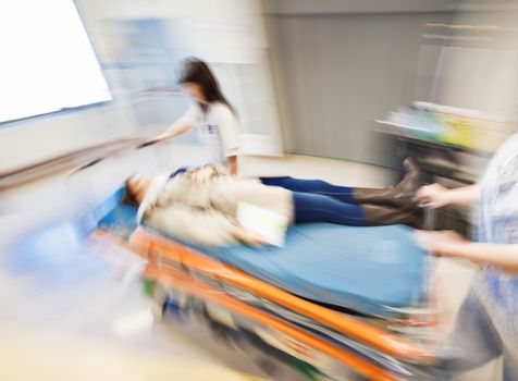 An emergency litter with patient, pushed fast through modern hospital corridor by two nurses. Panned, motion blurred picture.