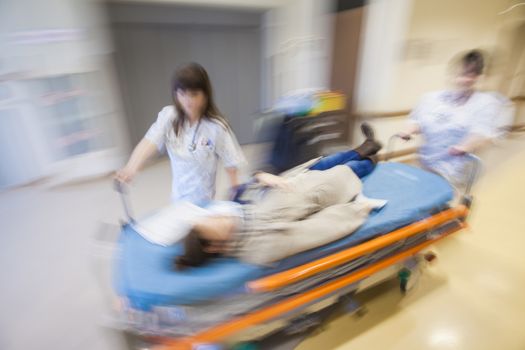 A litter with patient, pushed in emergency through modern hospital corridor by two nurses. Panned, motion blurred picture.