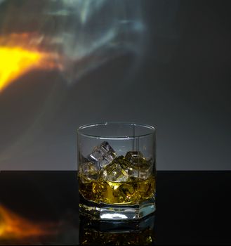 a glass of whiskey with ice on a black polished table