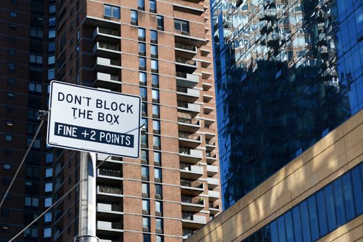 DON’T BLOCK THE BOX street sign in New York City, with diverse architecture of skyscrapers beyond